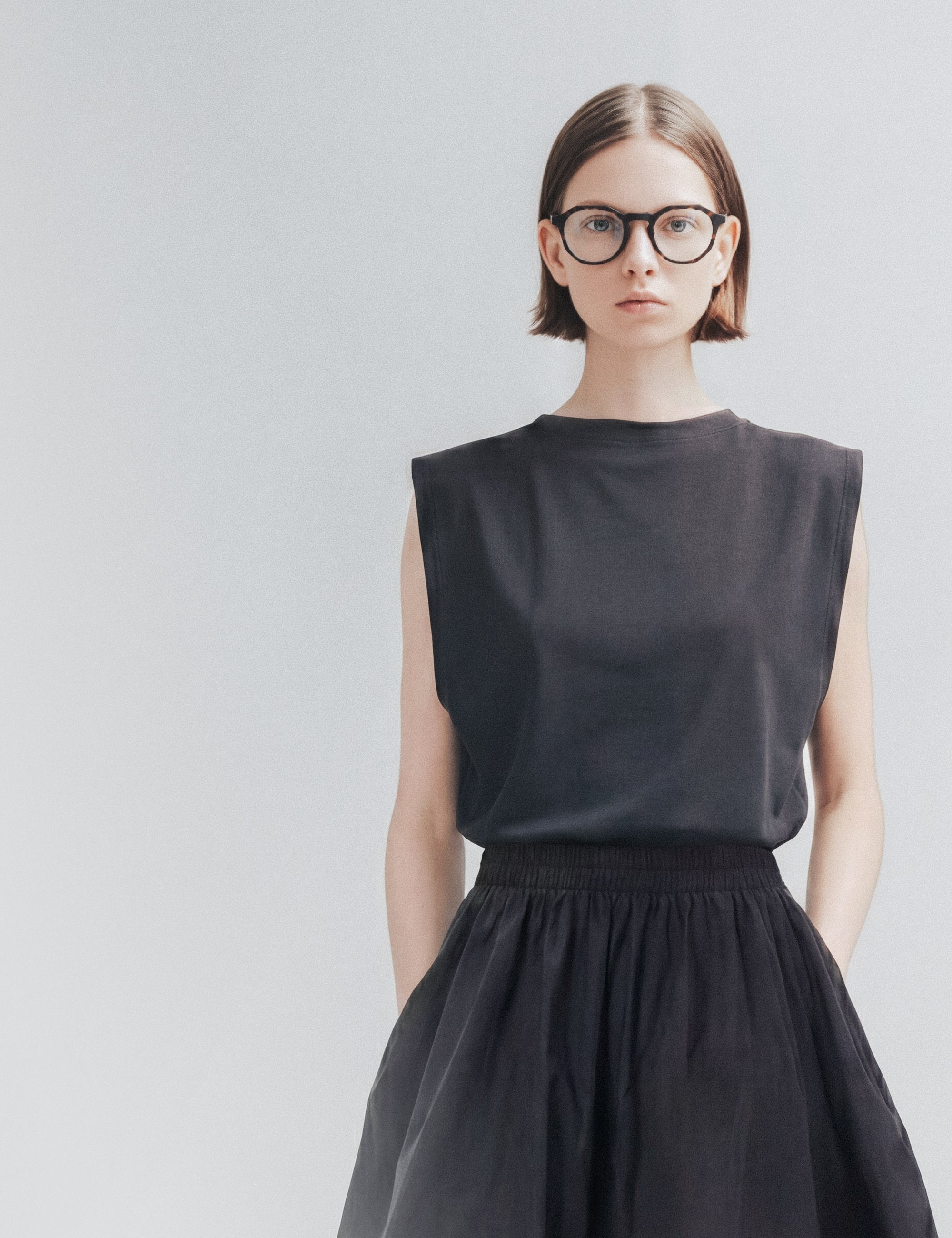 Editorial portrait, woman in glasses, sleeveless black top and full black skirt
