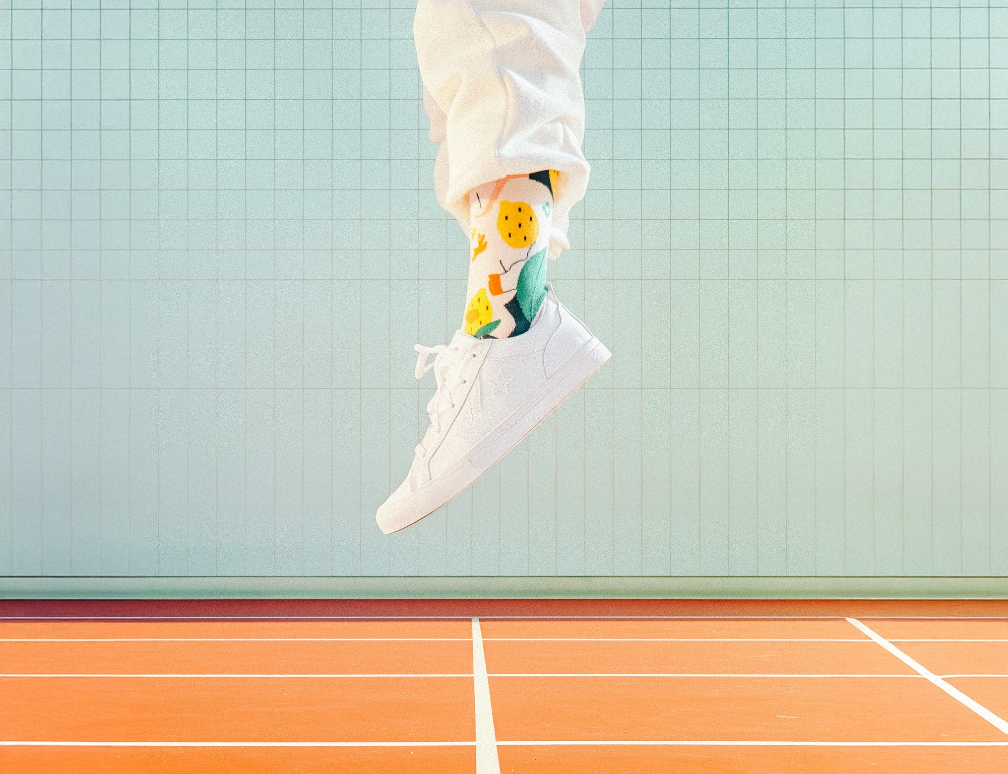 Person wearing colorful Limono Lemonheads socks and white sneakers on a tennis court
