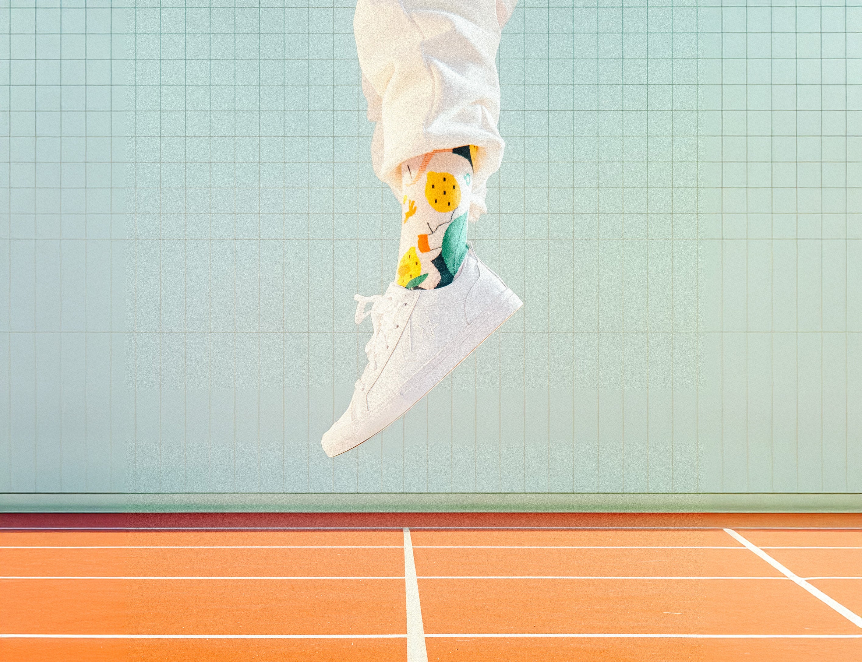 Person wearing colorful Limono Lemonheads socks and white sneakers on a tennis court