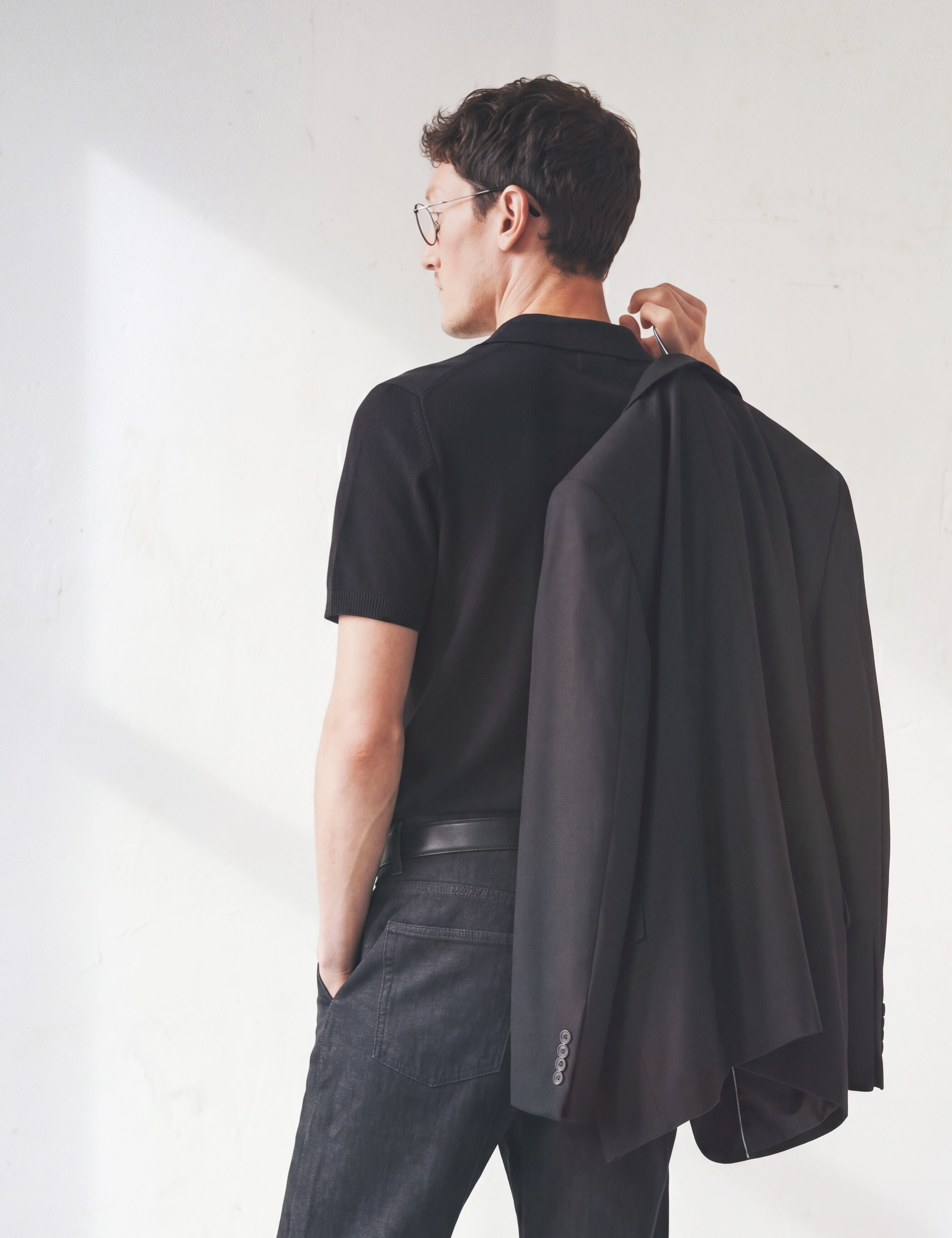 Limono Lemonheads Black lifestyle portrait, man in black polo holding a blazer over his shoulder