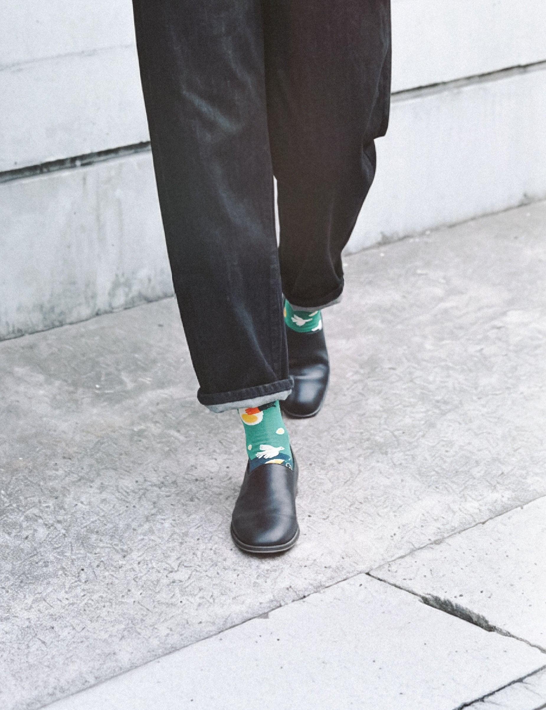 Cropped walk on sidewalk in dark jeans and leather boots with Limono Lemonheads Green socks peeking