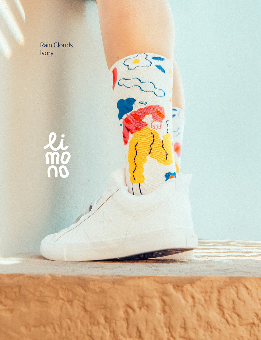 Limono Rain Clouds White socks with white Converse sneakers, sitting on a sandstone wall against pastel blue