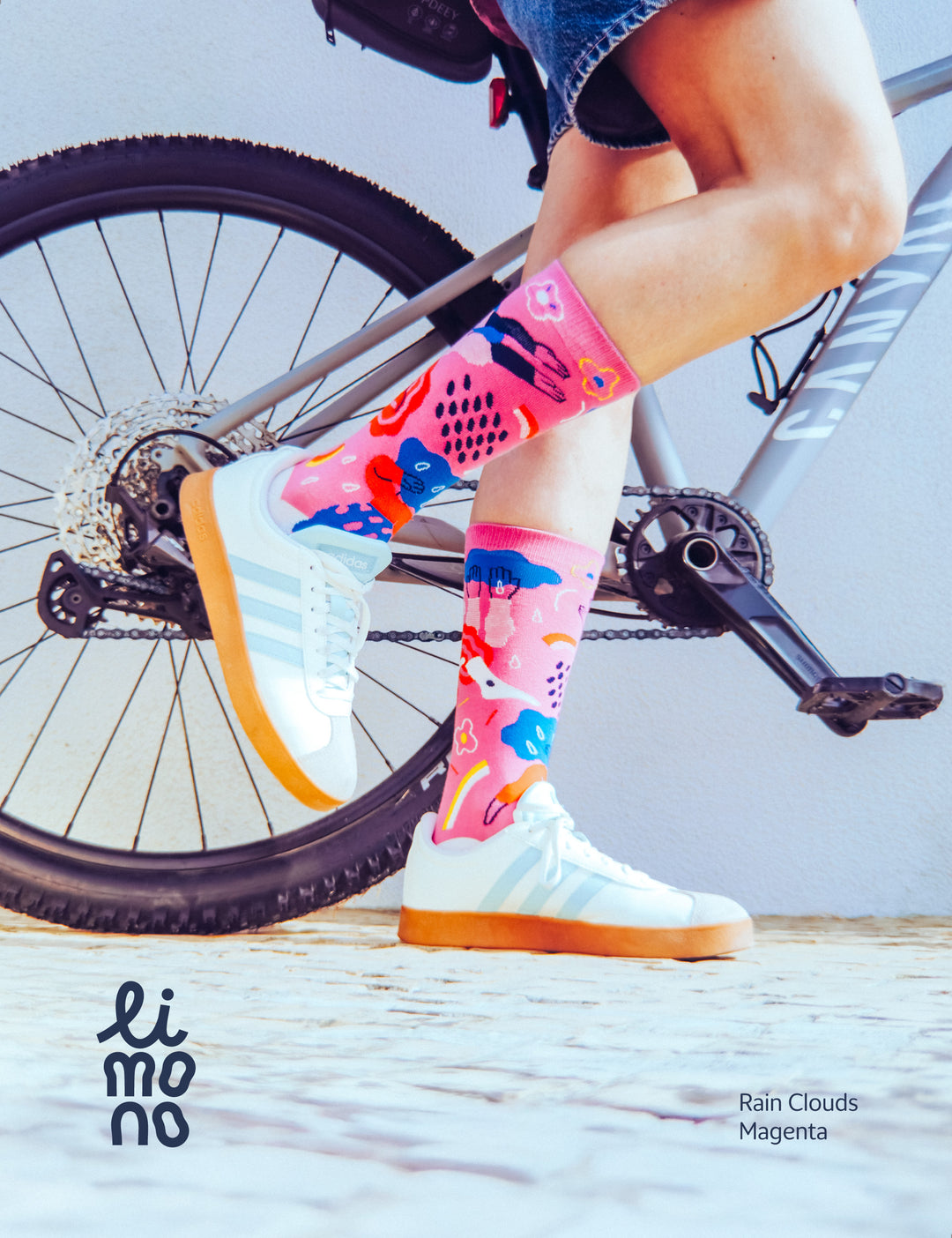 Person on bicycle wearing Limono Rain Clouds Magenta socks with white sneakers on cobblestone