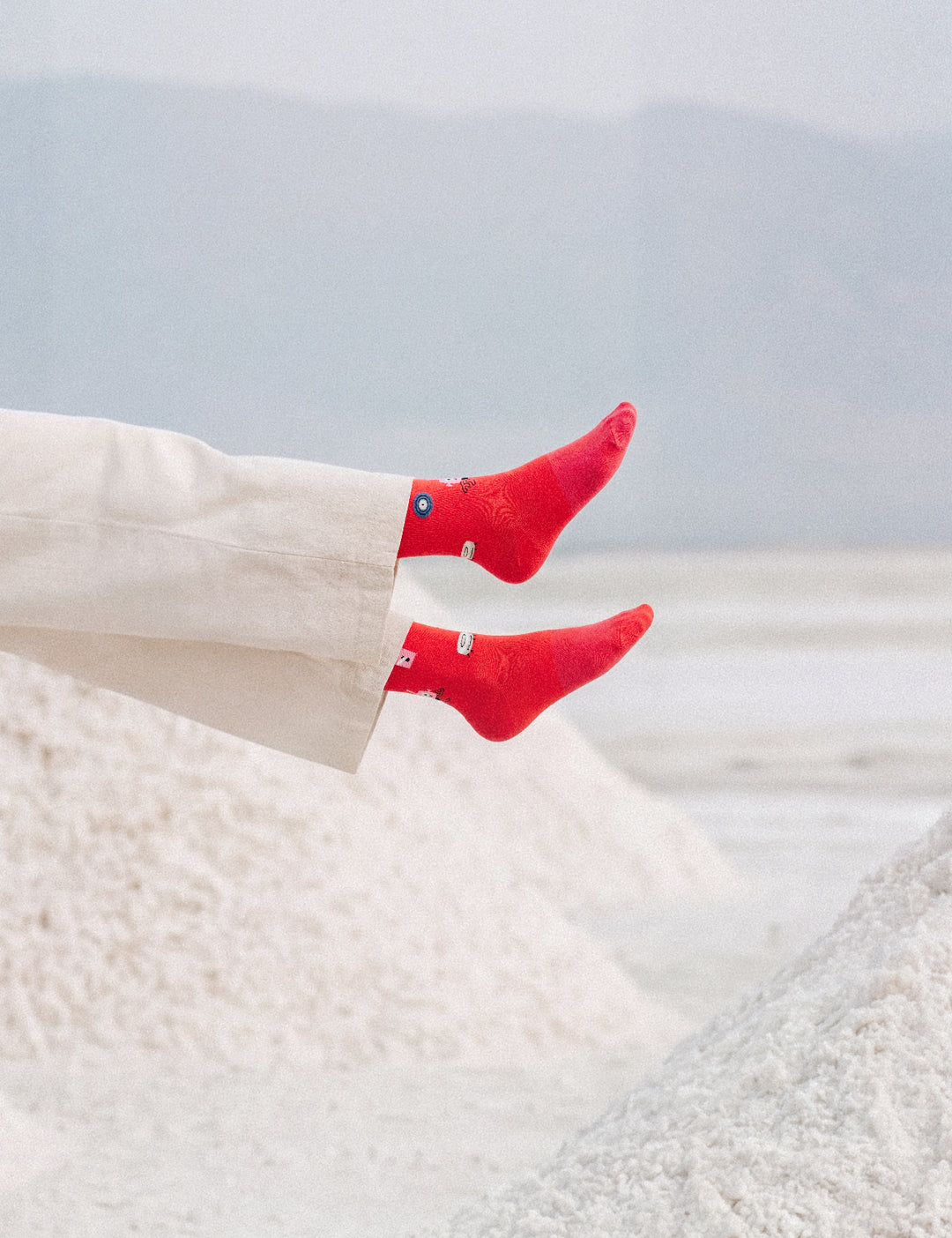 Limono Robots Day Red socks on legs in cream pants extended over salt mounds with mountains behind