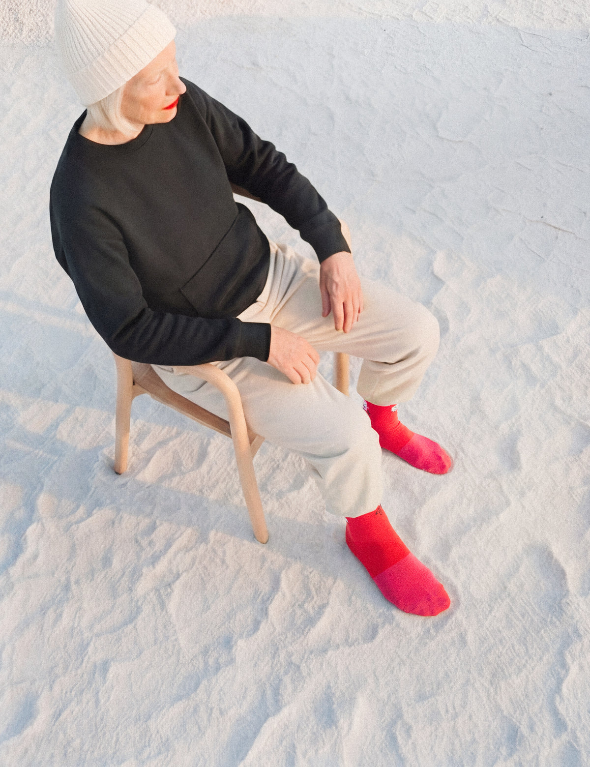 Limono Robots Day Red socks on a model in beanie and black sweater, seated in salt desert
