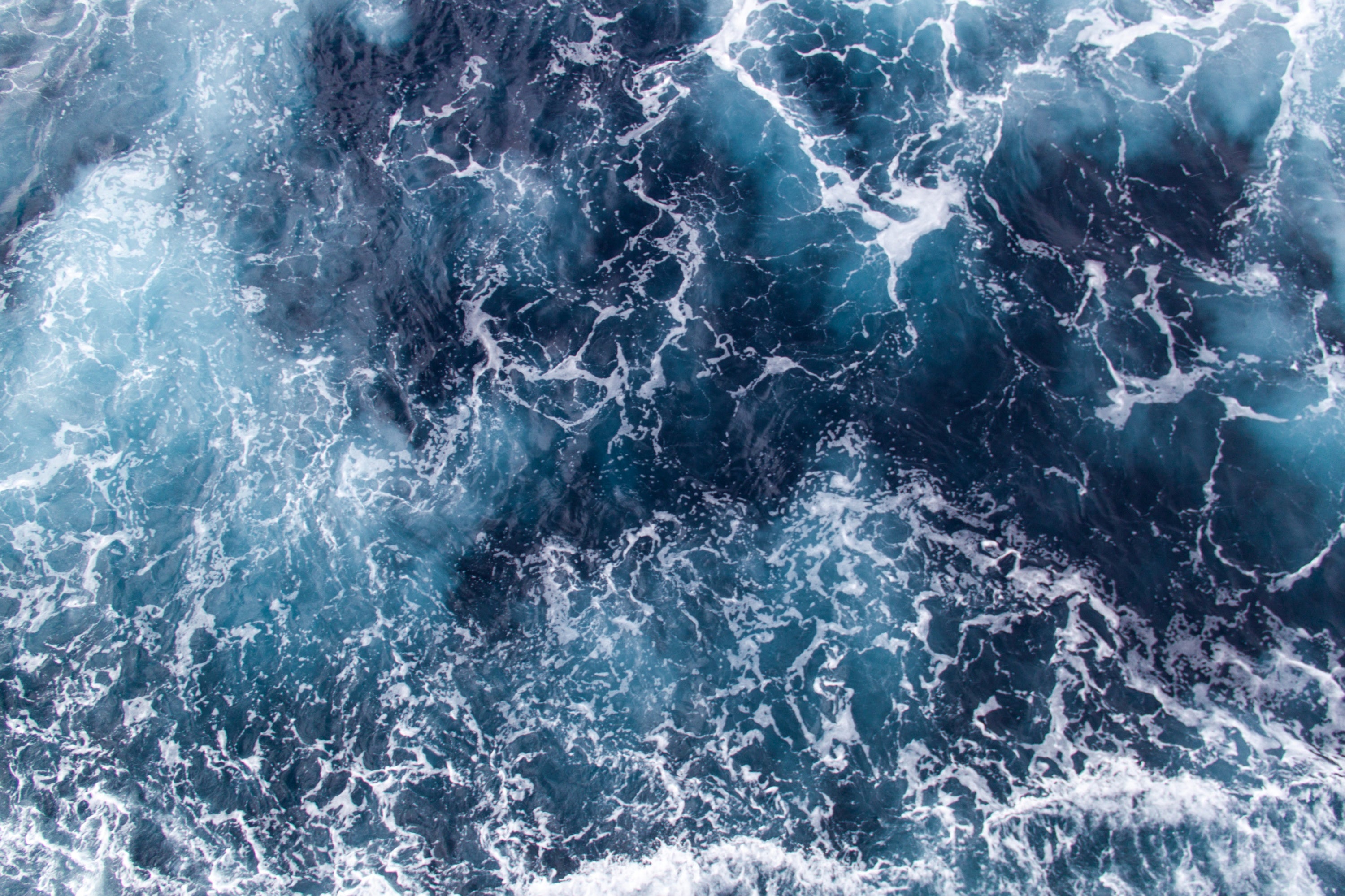 Aerial photo of churning blue ocean waves with white foam, abstract texture