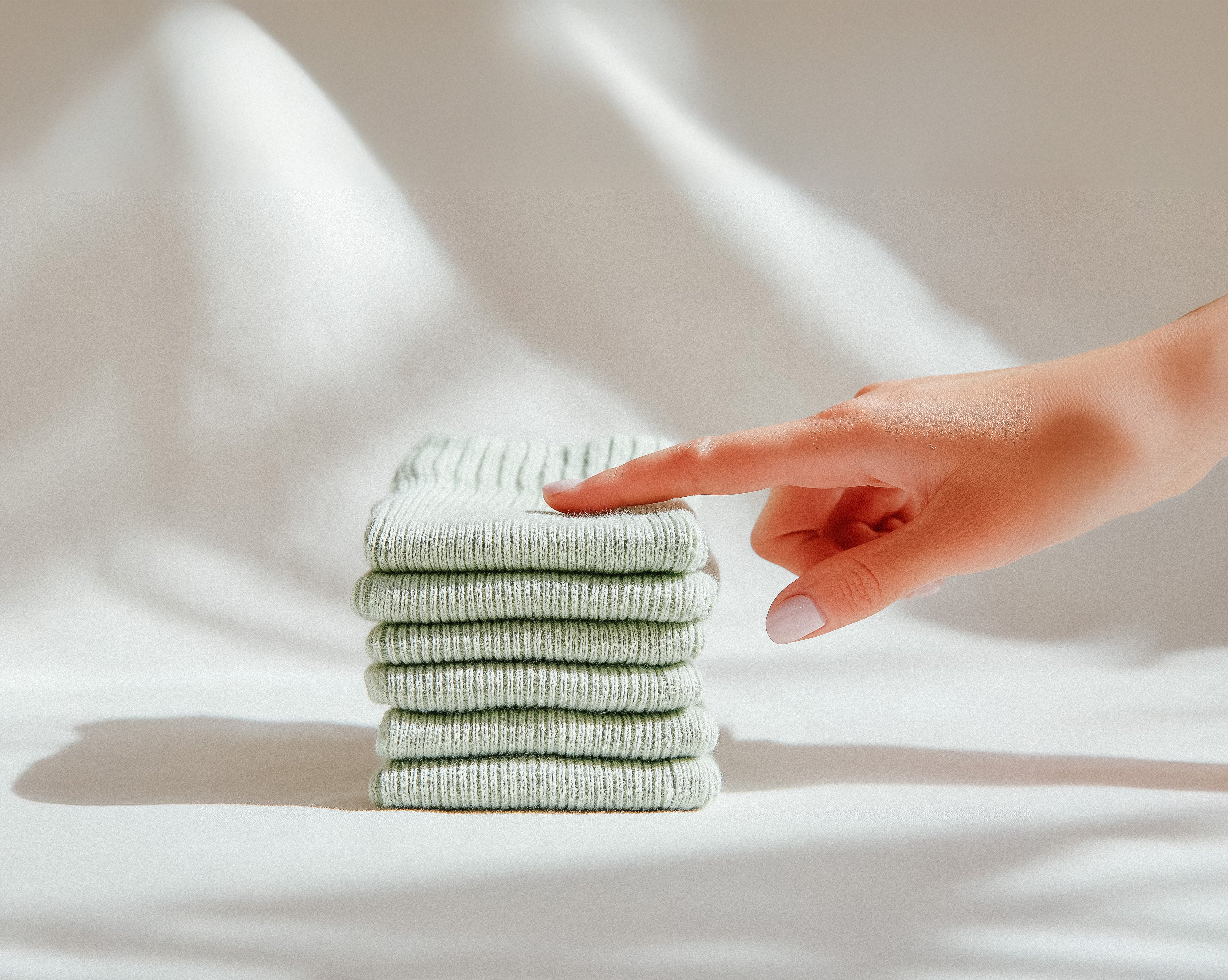 Limono socks. Stack of light green towels with a hand reaching out on a white background