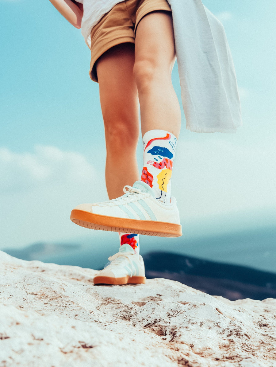 Limono Socks Rain Clouds collection. Model wearing bright pink illustrated socks, sitting on the ground next to a bicycle. Casual summer street photo shoot.