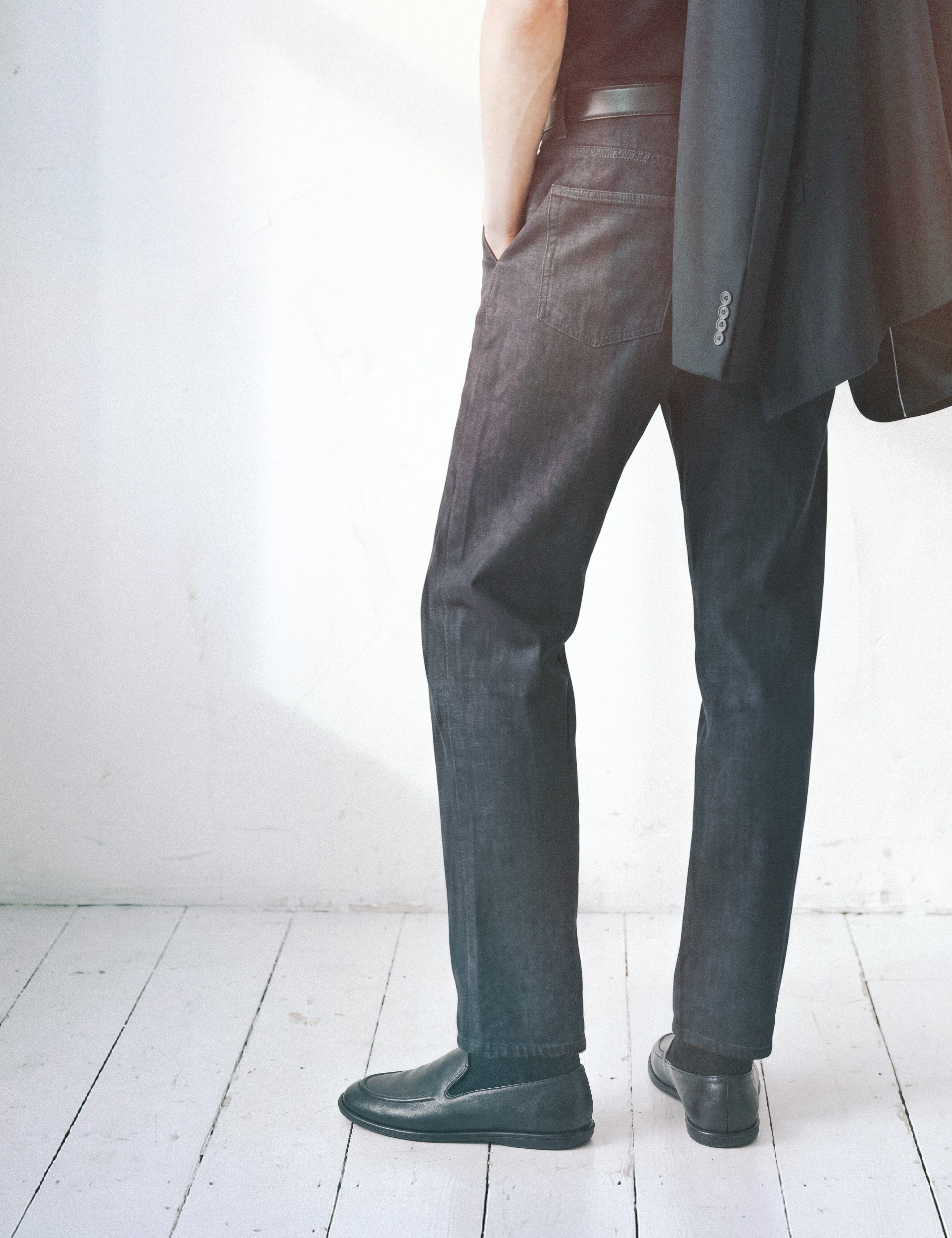 Editorial man back view in dark jeans with jacket over shoulder and leather flats on white floor