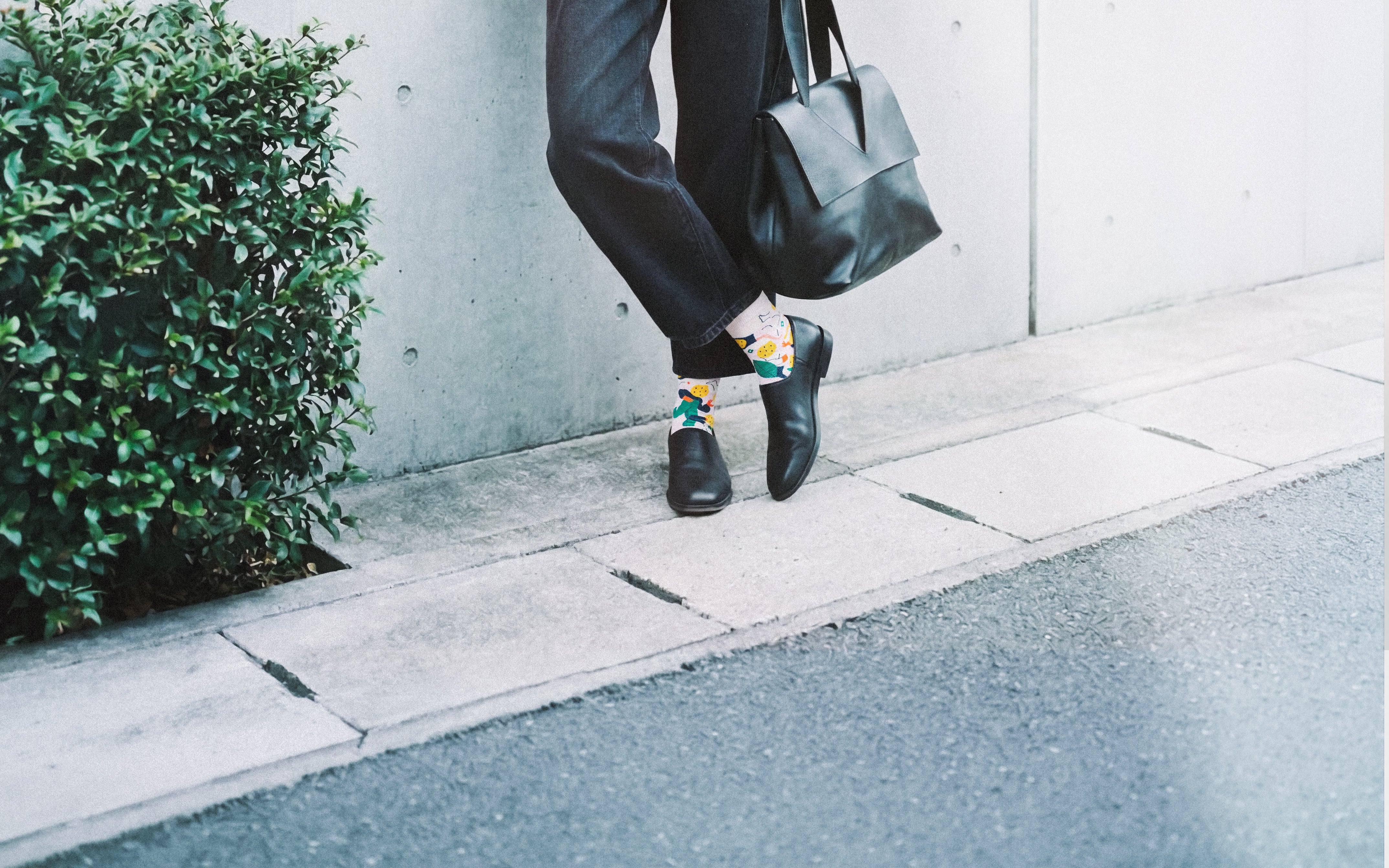 Woman cropped legs with leather tote on sidewalk by plant wearing Limono Lemonheads Rose socks