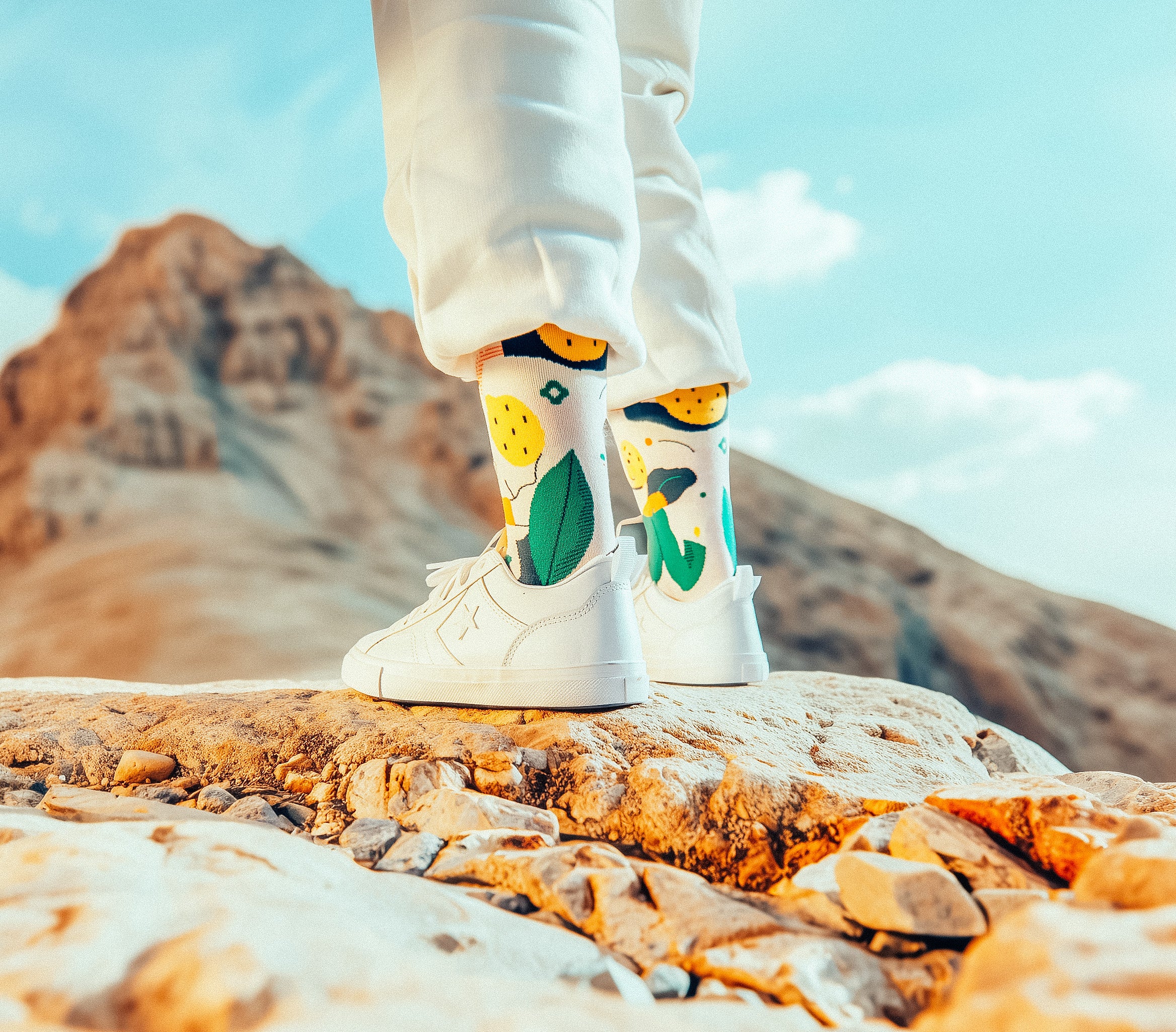 Person wearing Limono Lemonheads socks with colorful designs on a rocky surface with mountains in the background