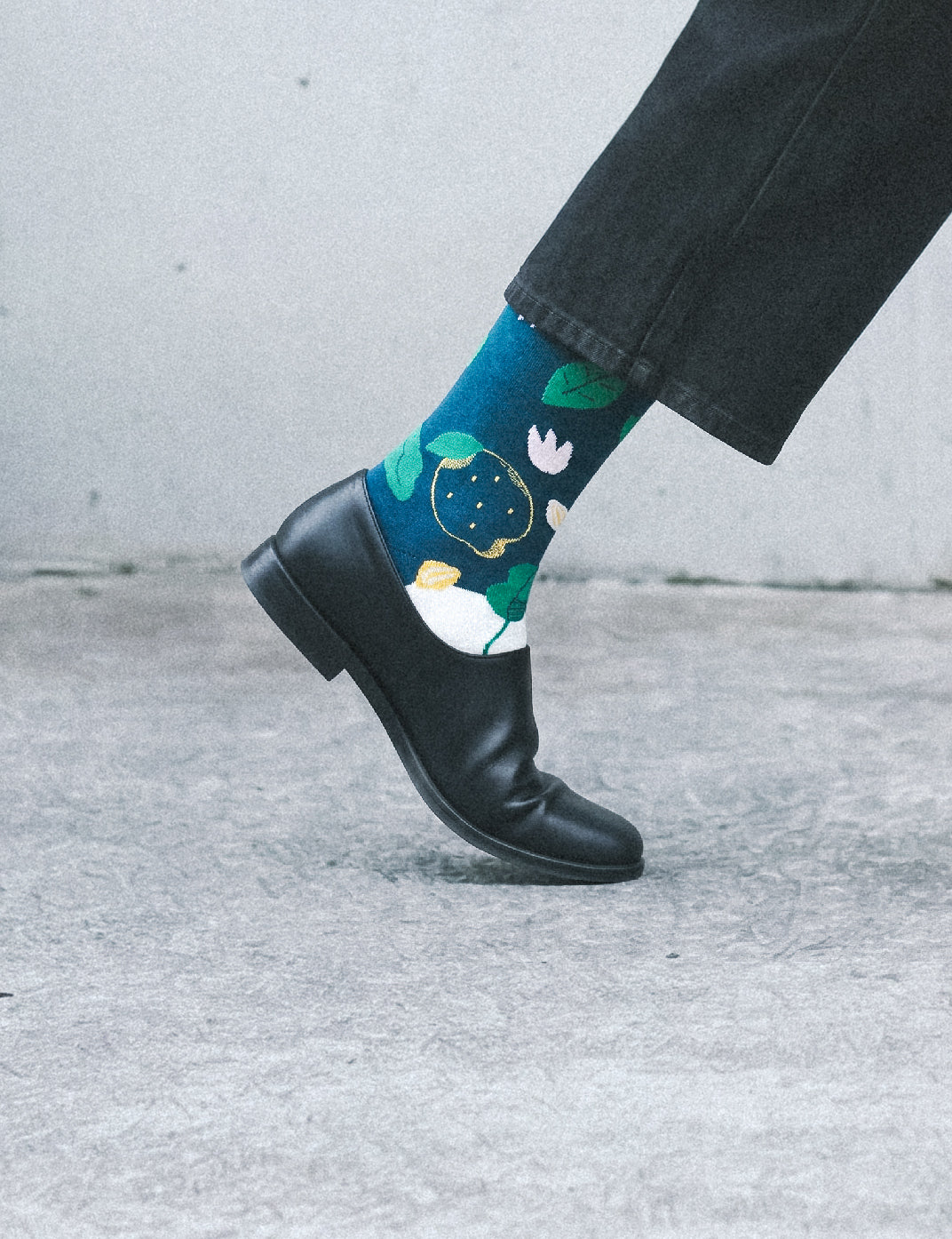 Cropped foot profile in dark trousers and leather boot wearing Limono Lemonheads Black sock