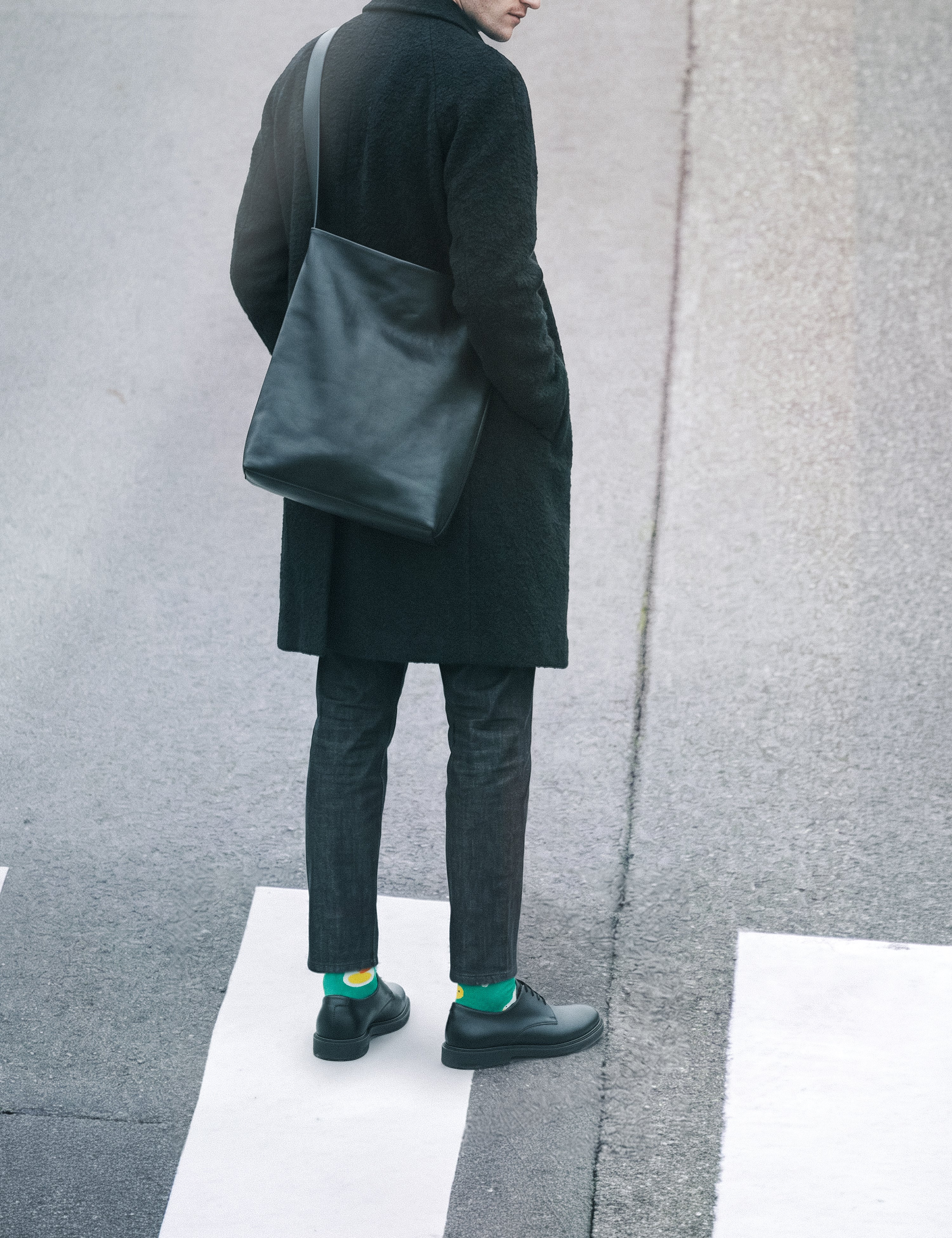 Man back view in long dark coat with leather bag at crosswalk wearing Limono Lemonheads Green socks