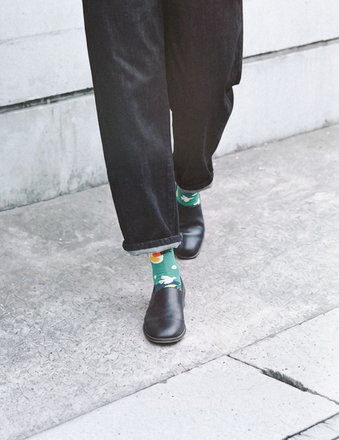 Cropped walk on sidewalk in dark jeans and leather boots with Limono Lemonheads Green socks peeking