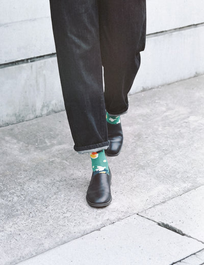 Cropped walk on sidewalk in dark jeans and leather boots with Limono Lemonheads Green socks peeking