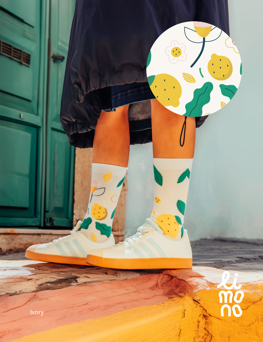 Limono Lemonheads Ivory socks worn with cream sneakers on warm stone surface against green door