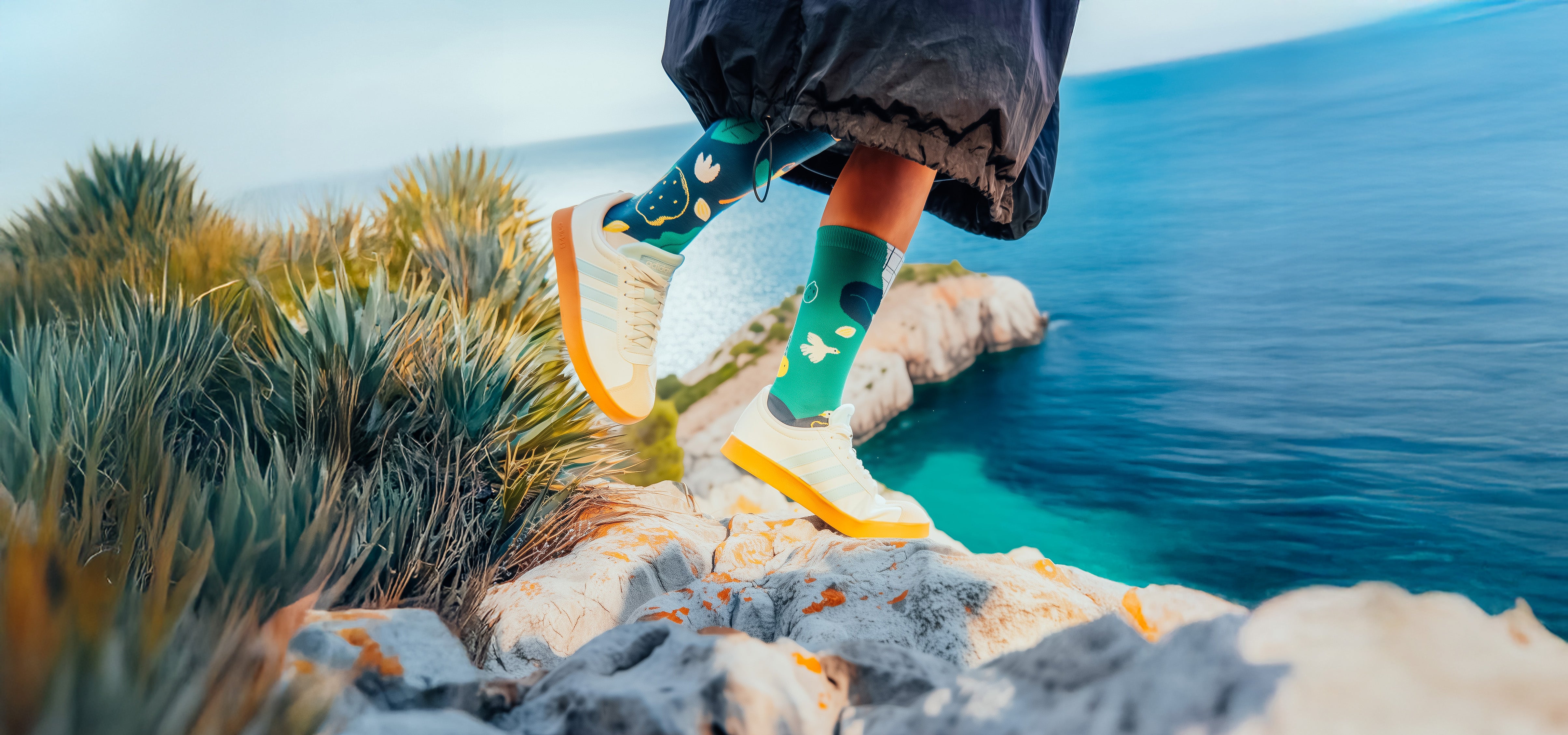Person standing on a rocky outcrop by a body of water wearing colorful Limono socks.