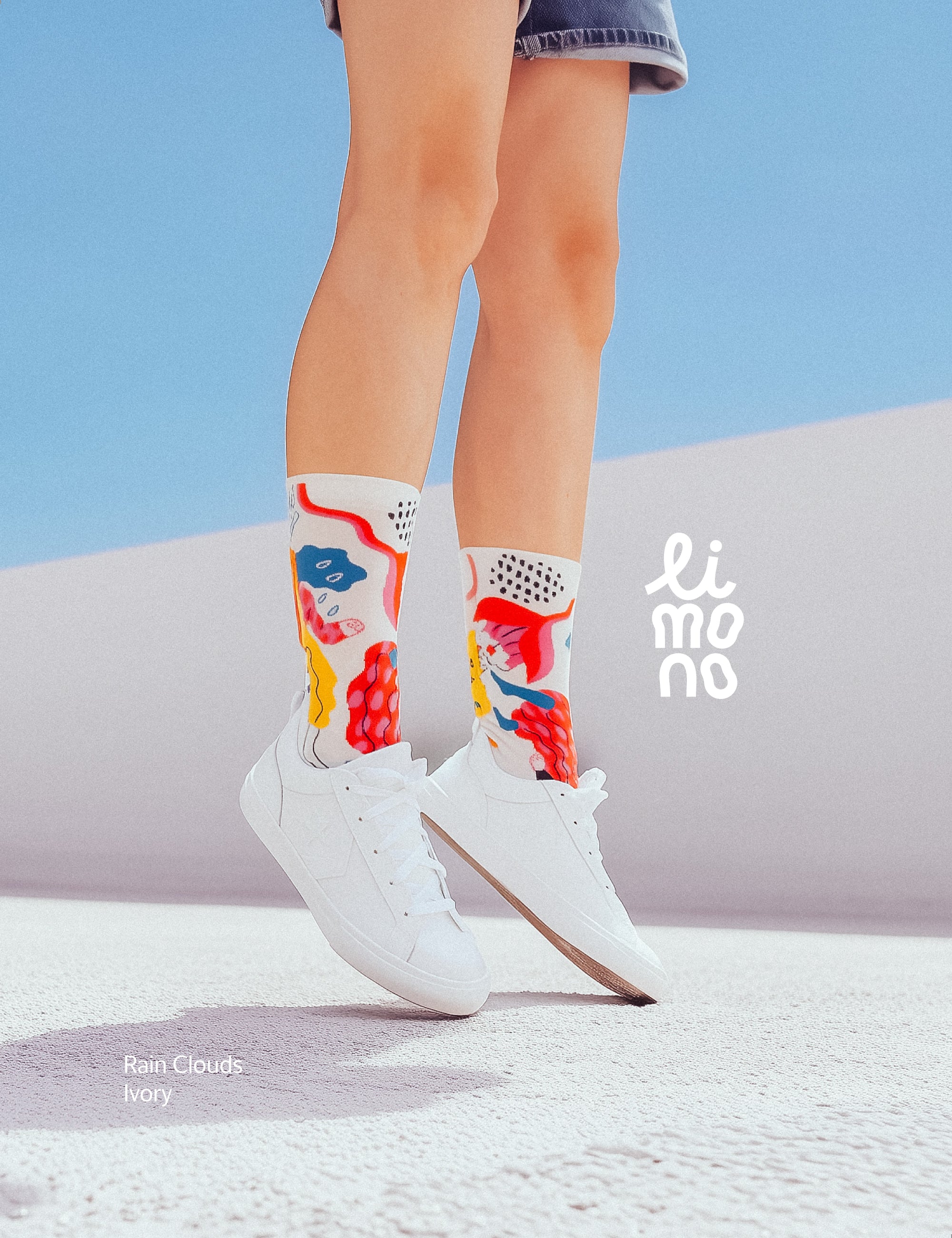 Lifestyle jump shot against blue sky and pastel curve, wearing Limono Rain Clouds White socks with white sneakers
