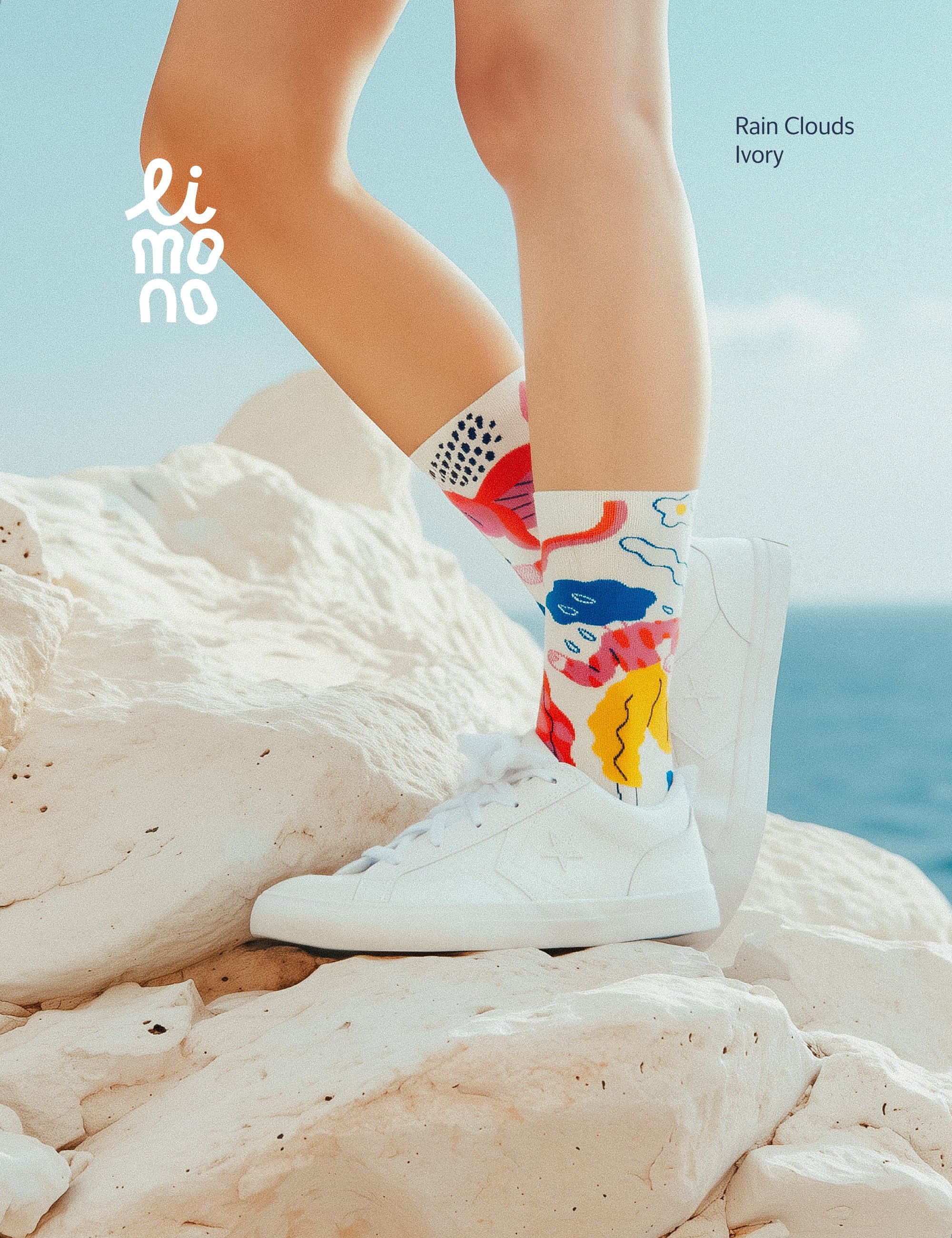 Lifestyle photo by the sea on white limestone rocks, wearing Limono Rain Clouds White socks and white sneakers