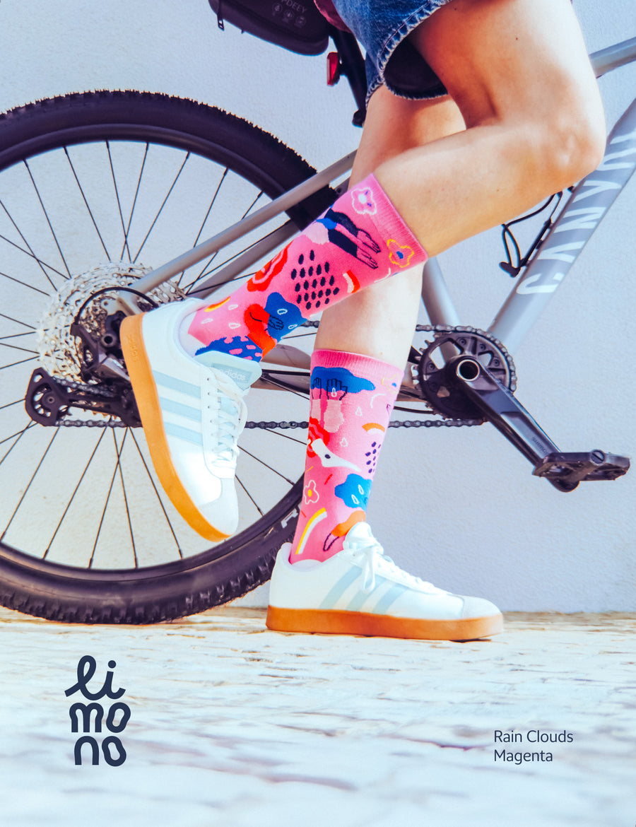 Person on bicycle wearing Limono Rain Clouds Magenta socks with white sneakers on cobblestone