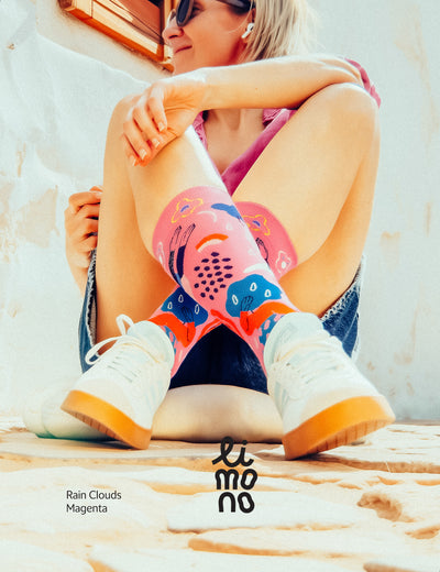 Woman in pink top and denim shorts sitting outdoors in sunglasses, wearing Limono Rain Clouds Magenta socks