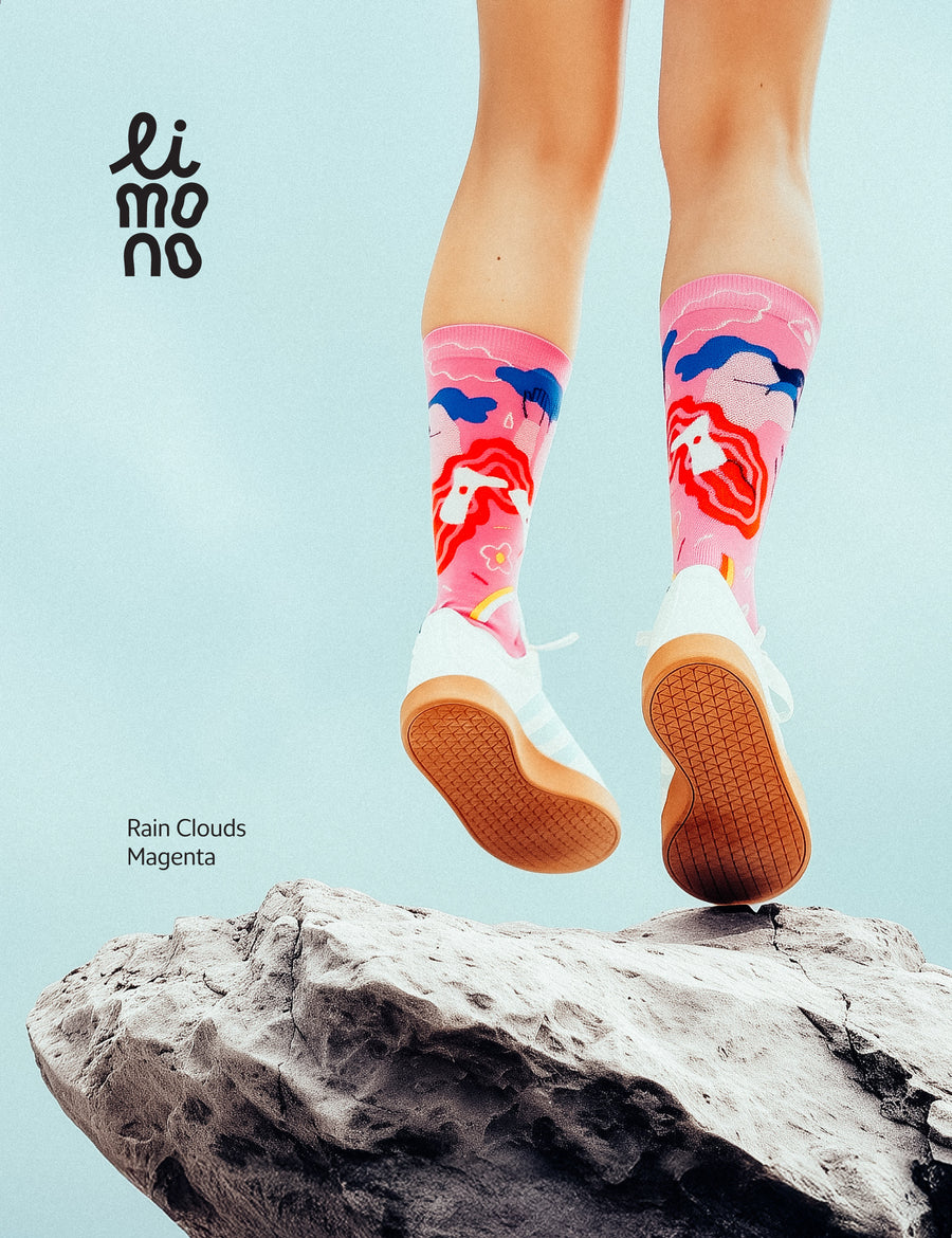 Lifestyle jump shot above a rock against light sky, wearing Limono Rain Clouds Magenta socks and white sneakers
