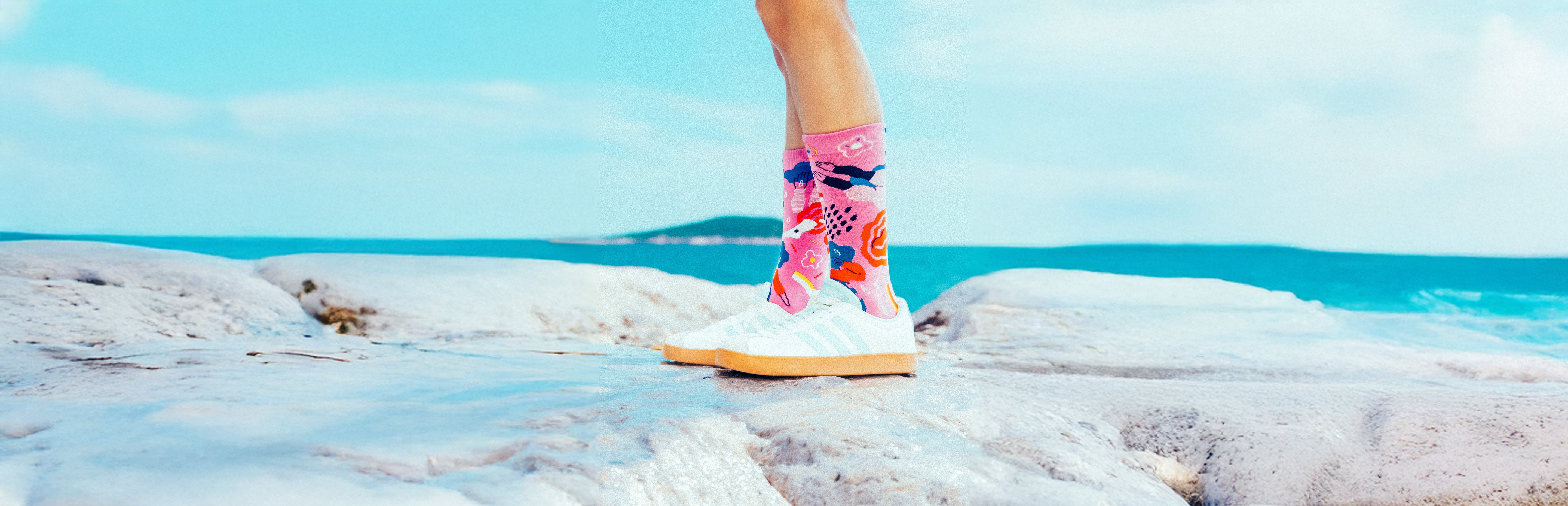 Person wearing colorful Limono Rain Clouds socks on a rocky beach with ocean and sky in the background