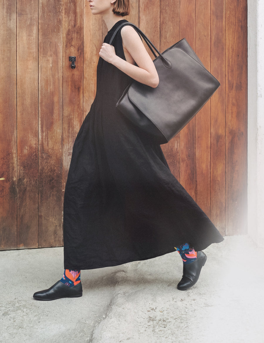 Woman in long black dress with leather tote walking by a wooden door, wearing Limono Rain Clouds Black socks