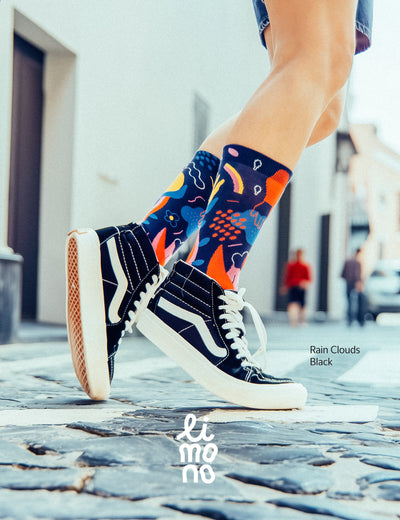 Person walking on cobblestone street in black Vans high-tops, wearing Limono Rain Clouds Black socks