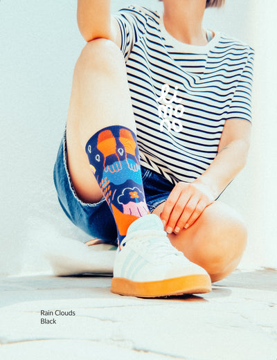 Woman in striped tee and denim shorts sitting outdoors, wearing Limono Rain Clouds Black socks with white sneakers