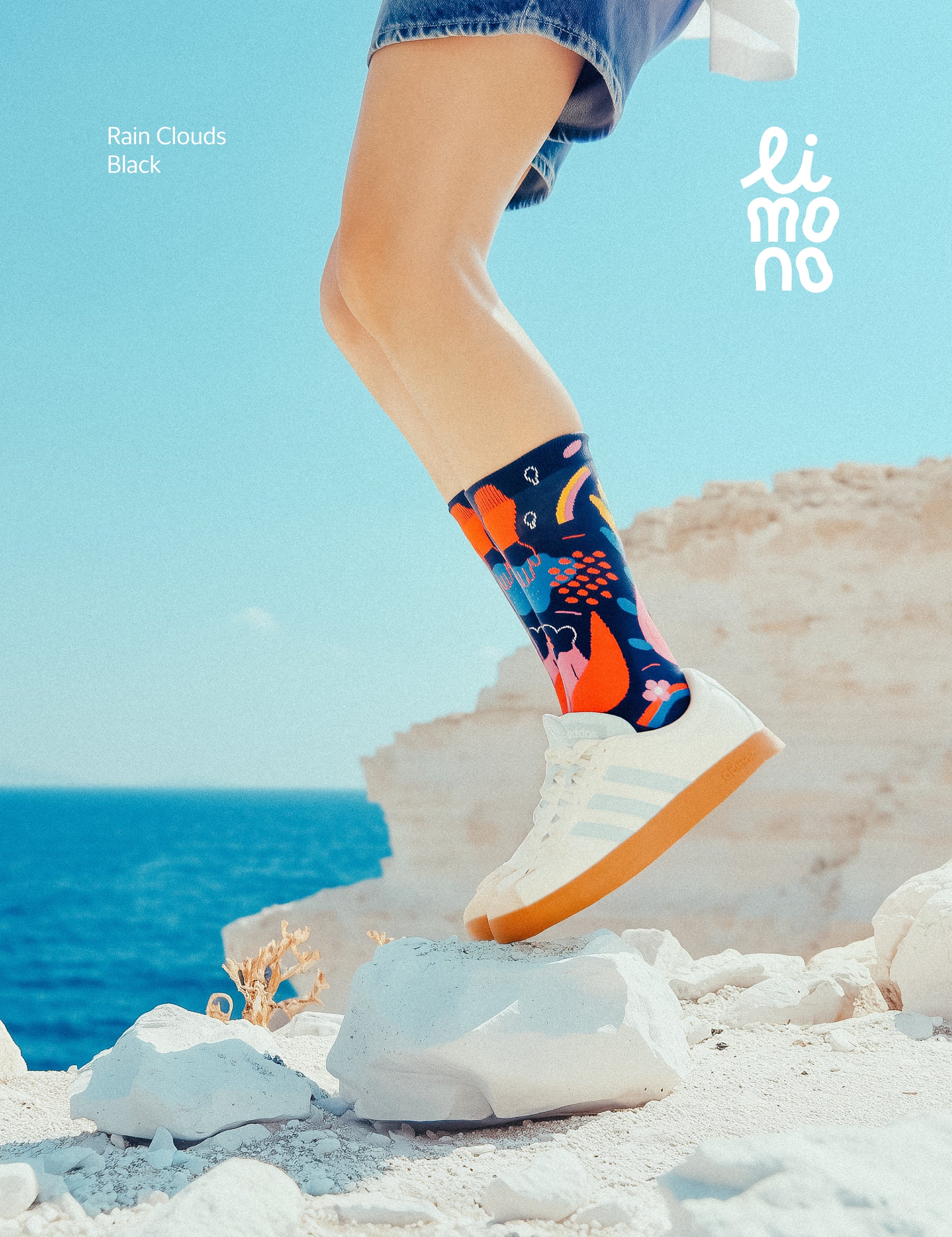 Limono Socks Rain Clouds collection. Illustrated socks on trend made in Portugal. Organic combed cotton. Person wearing colorful socks with a blue sky and ocean background, featuring the brand 'limo'.