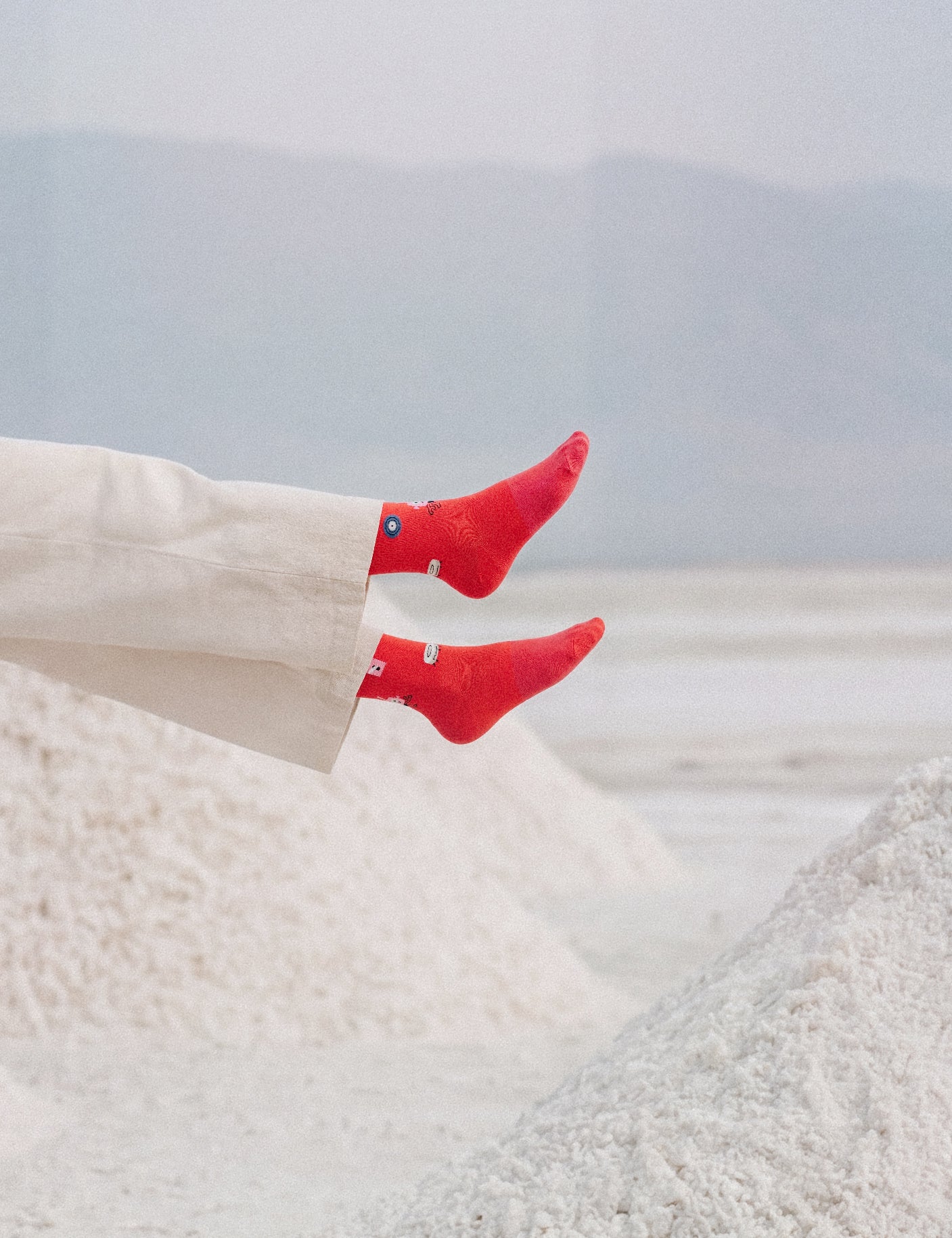 Limono Robots Day Red socks on a model in white beanie levitating above salt mounds, vertical crop