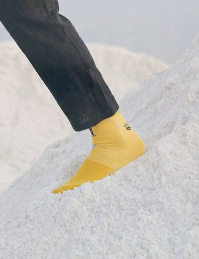 Limono Robots Day Yellow socks worn by a model stepping into a salt mound, dark trousers above
