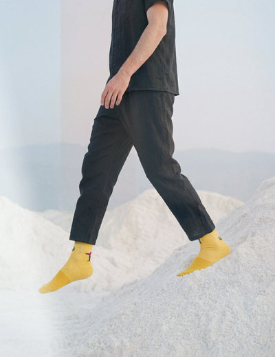 Limono Robots Day Yellow socks on a model in a styled lifestyle scene with salt mounds