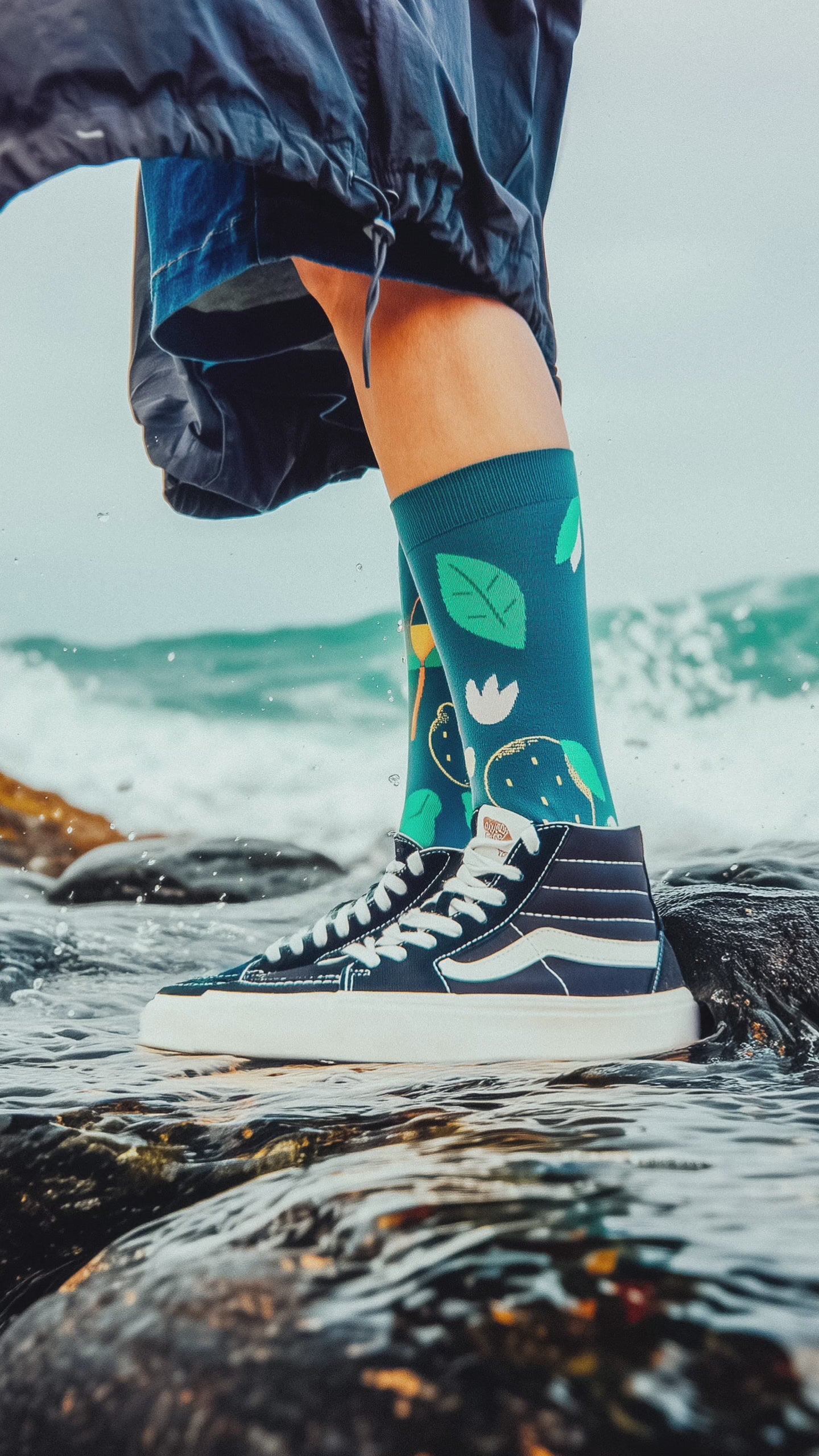 Load video: Limono Socks Lemonheads collection. Illustrated socks on trend made in Portugal. Organic combed cotton. Person wearing colorful socks and high-top sneakers on a rocky shoreline with ocean waves.